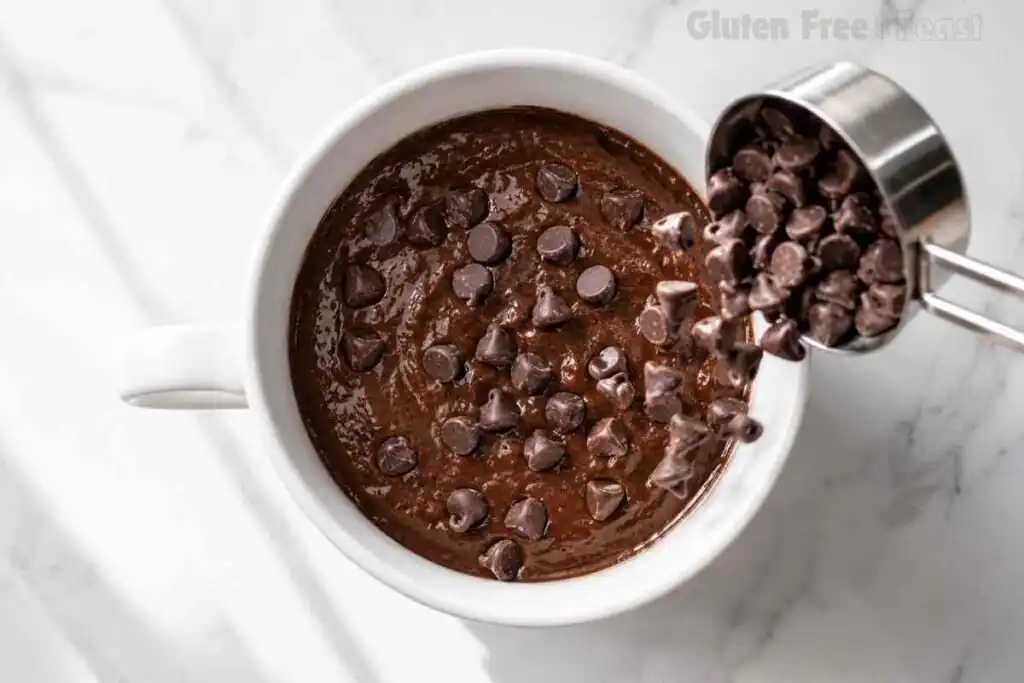 Chocolate chips being poured into gluten-free chocolate mug cake batter