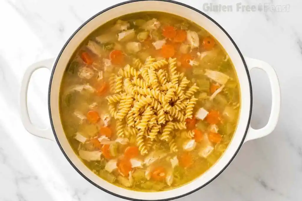 Gluten-free rotini pasta added to chicken noodle soup in a Dutch oven.