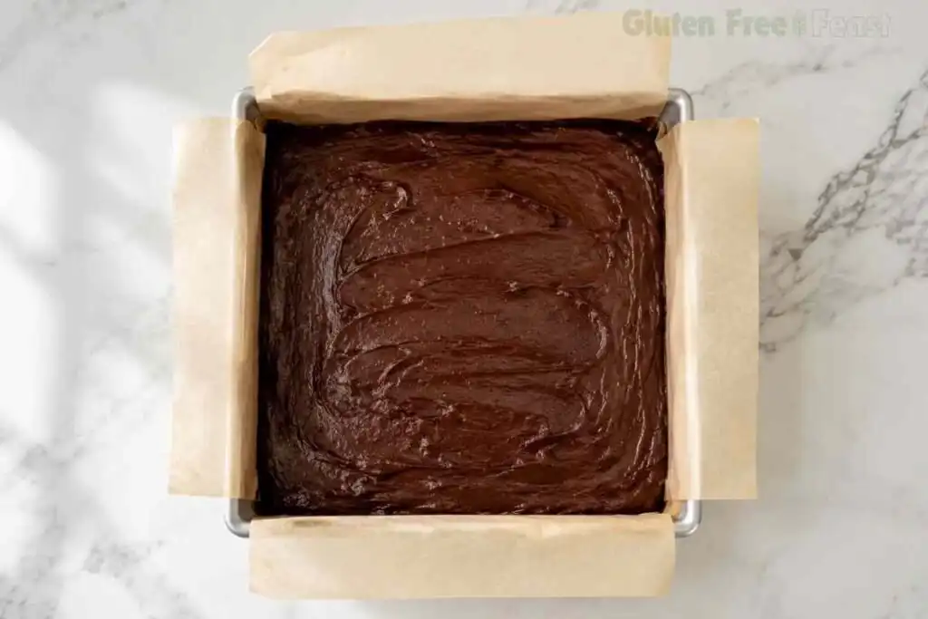 Gluten-free brownie batter spread evenly in a parchment-lined square baking pan