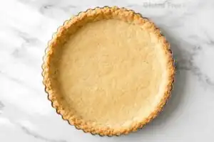 Fully baked gluten free pie crust in a fluted tart pan on white marble