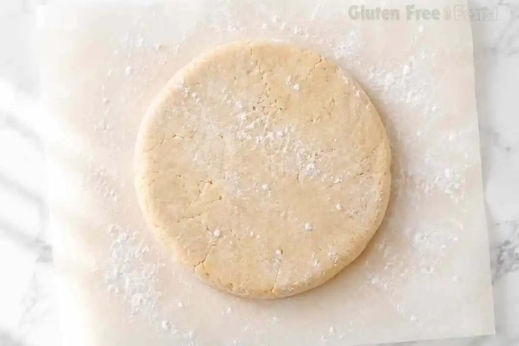 Gluten free pie dough disc lightly floured on parchment paper