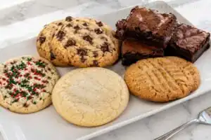 Assortment of gluten free dessert recipes on a white rectangular platter — chocolate chip cookies, fudgy brownies, Christmas sprinkle cookies, a sugar cookie, and a peanut butter cookie on a marble surface