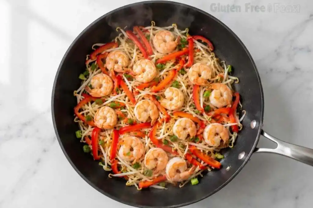 Shrimp, bean sprouts, and red peppers sautéing in a skillet