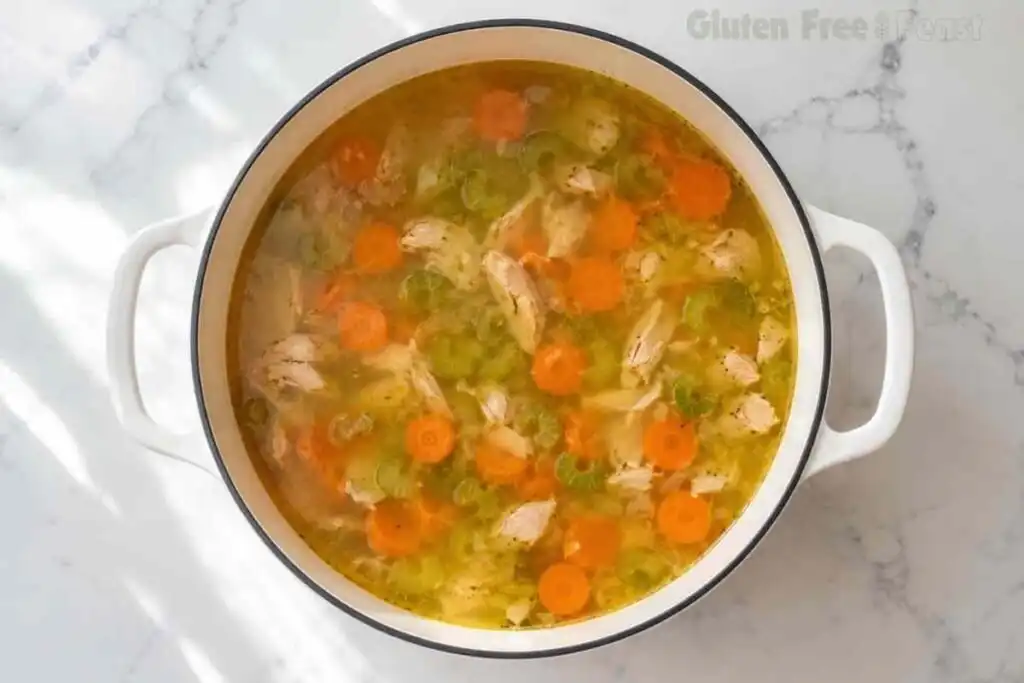 Gluten-free chicken soup simmering with chicken, carrots, celery, and broth in a Dutch oven.