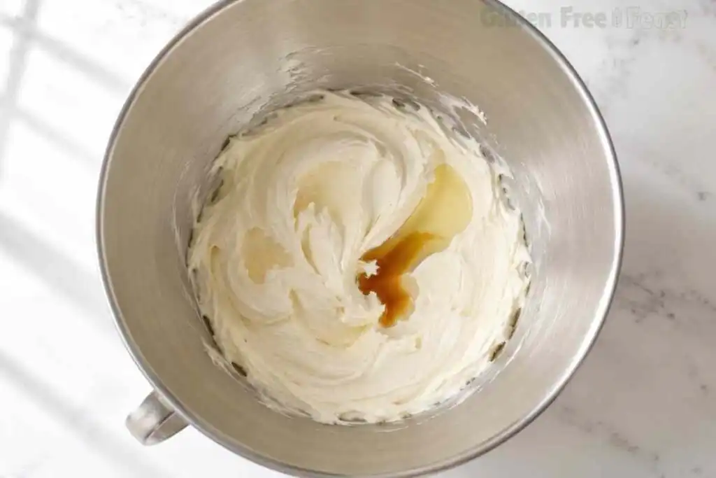 Vanilla and lemon juice added to cream cheese frosting in a stainless steel bowl.
