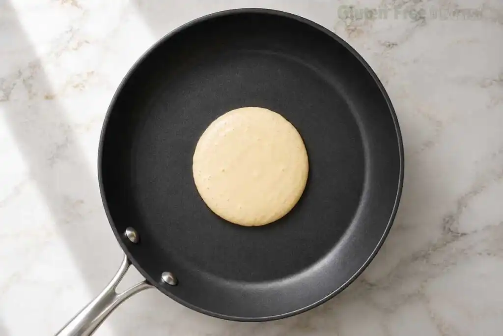 Pouring a 1/4 cup of rested gluten-free pancake batter onto a buttered nonstick skillet over medium heat.