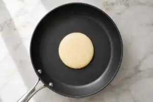Pouring a 1/4 cup of rested gluten-free pancake batter onto a buttered nonstick skillet over medium heat.