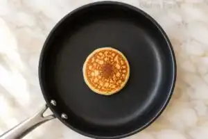 A perfectly golden-brown, fluffy gluten-free pancake cooking in a skillet after being flipped once.