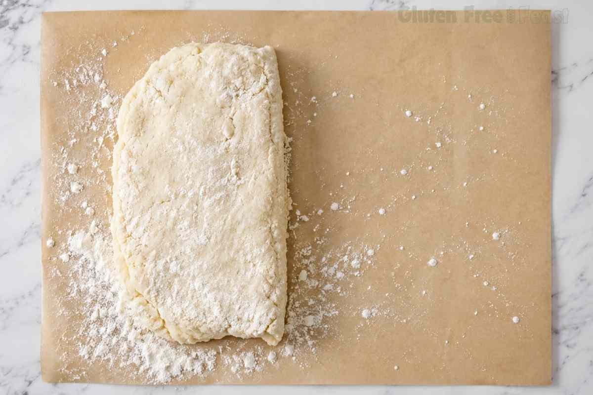Gluten free biscuit dough folded over once on floured parchment paper to begin creating flaky buttery layers