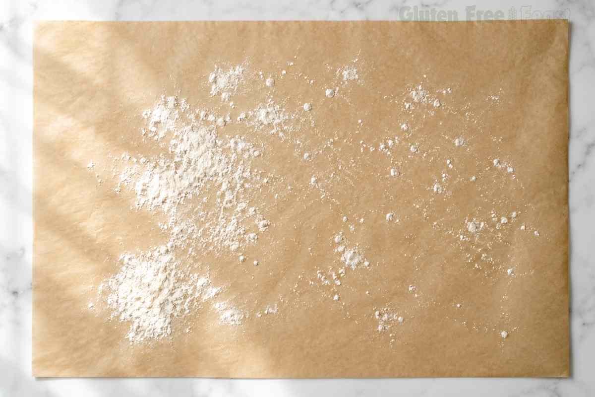 Parchment paper lightly dusted with gluten free flour on a marble surface prepared for shaping gluten free biscuit dough