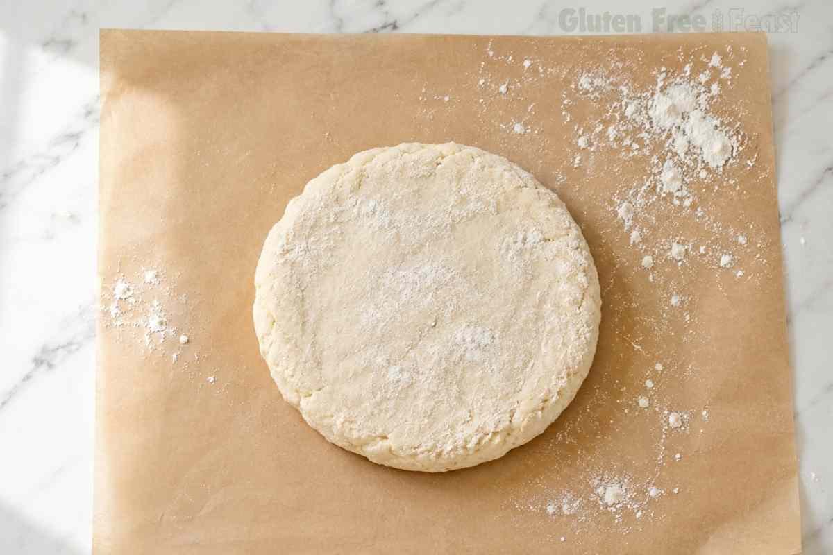 Gluten free biscuit dough patted into a smooth round disk on floured parchment paper ready to cut into biscuit rounds