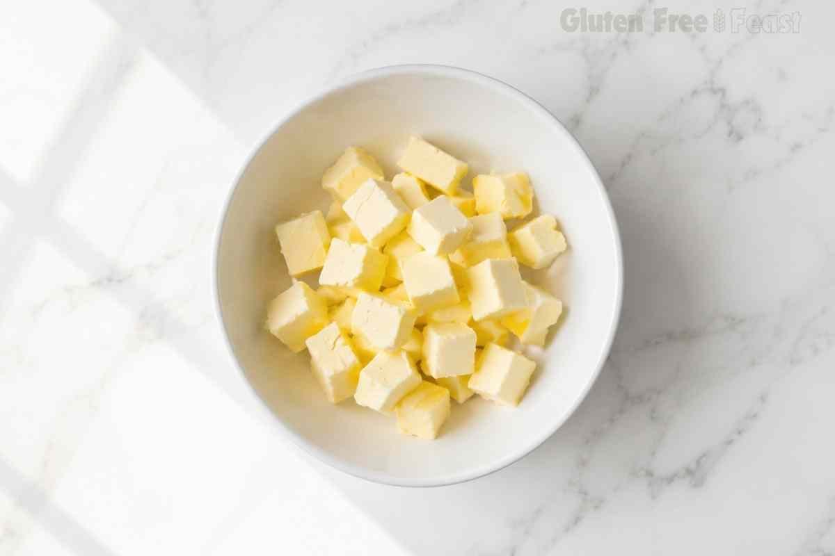 Cold butter cut into small cubes in a white bowl on marble ready to be cut into the gluten free biscuit flour mixture