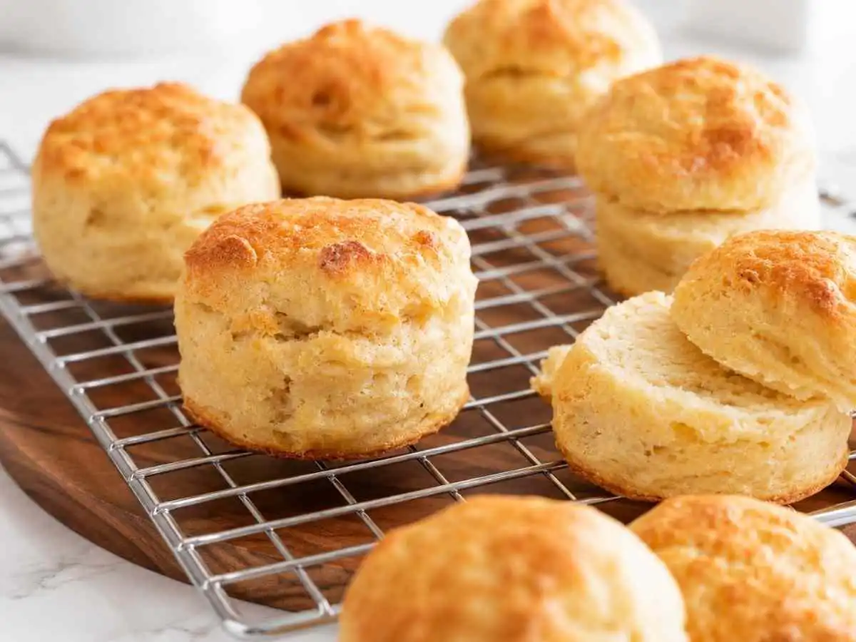Gluten free buttermilk biscuits on a cooling rack with one biscuit split open showing soft flaky layers inside