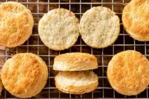 Gluten-Free Buttermilk Biscuits (Soft, Fluffy, and Celiac-Safe) Overhead view of gluten free buttermilk biscuits on a wire rack with one biscuit split open revealing the fluffy celiac safe interior