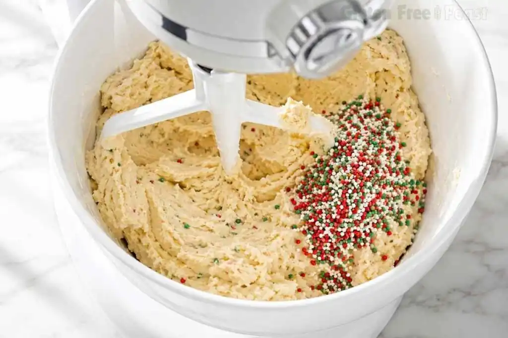 Red green and white sprinkles being folded into gluten free Christmas cookie dough in a stand mixer