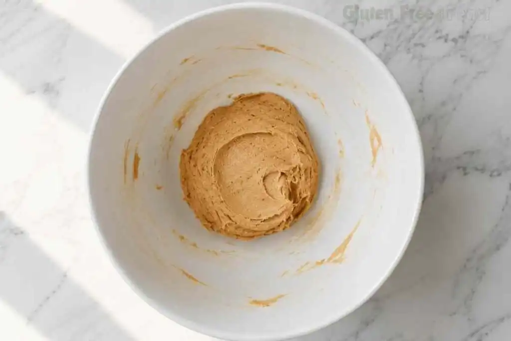 Gluten free peanut butter cookie dough formed into a smooth ball in a large white ceramic bowl on marble ready to refrigerate for 30 minutes before baking