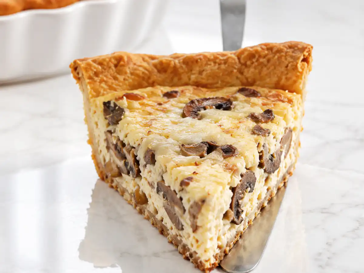 Close up of a slice of gluten free quiche on a pie server showing the creamy egg custard filling packed with mushrooms and a golden flaky crust