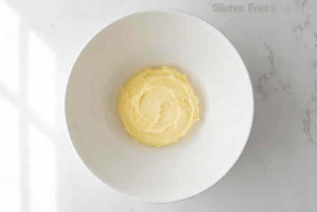 Butter beaten smooth and pale in a white bowl before creaming with sugar for gluten free sugar cookies