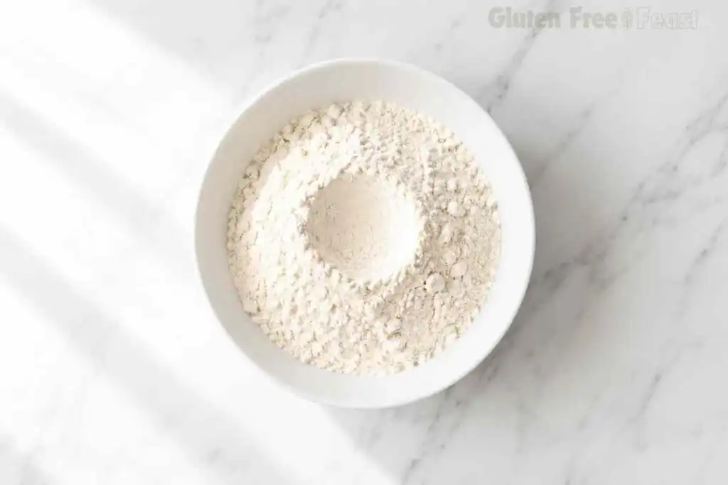 Certified gluten free flour blend and baking powder whisked together in a white bowl on marble