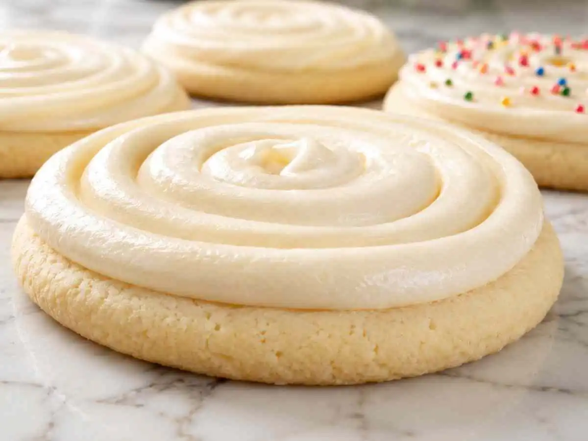 Gluten free sugar cookies with swirled white buttercream frosting on a marble surface, one topped with colorful sprinkles