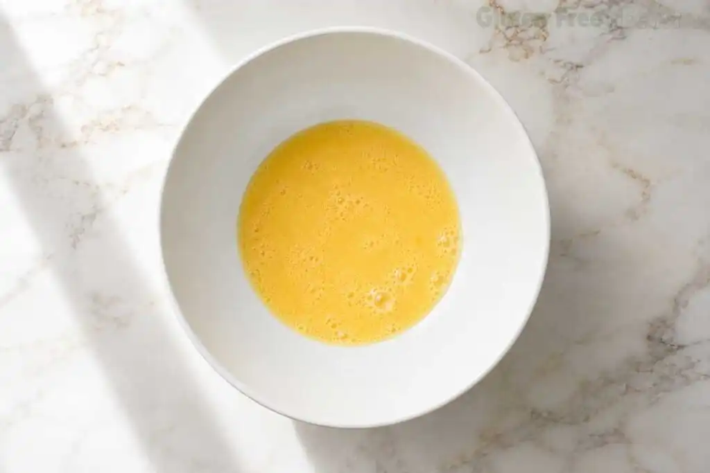 Whisking room-temperature milk, egg, melted butter, and vanilla extract in a white bowl for gluten-free pancake batter.