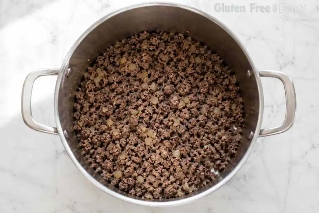 Browned ground beef cooking in a stainless steel pot for gluten free chili.