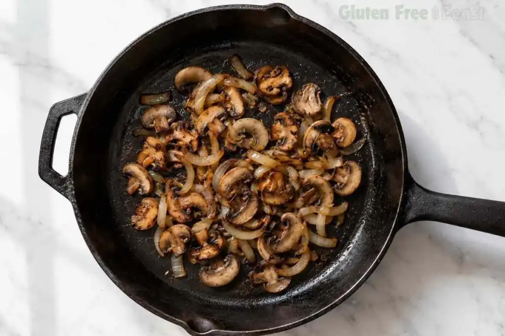 Golden brown mushrooms and onions cooking in a skillet for Gluten Free Beef Stroganoff.