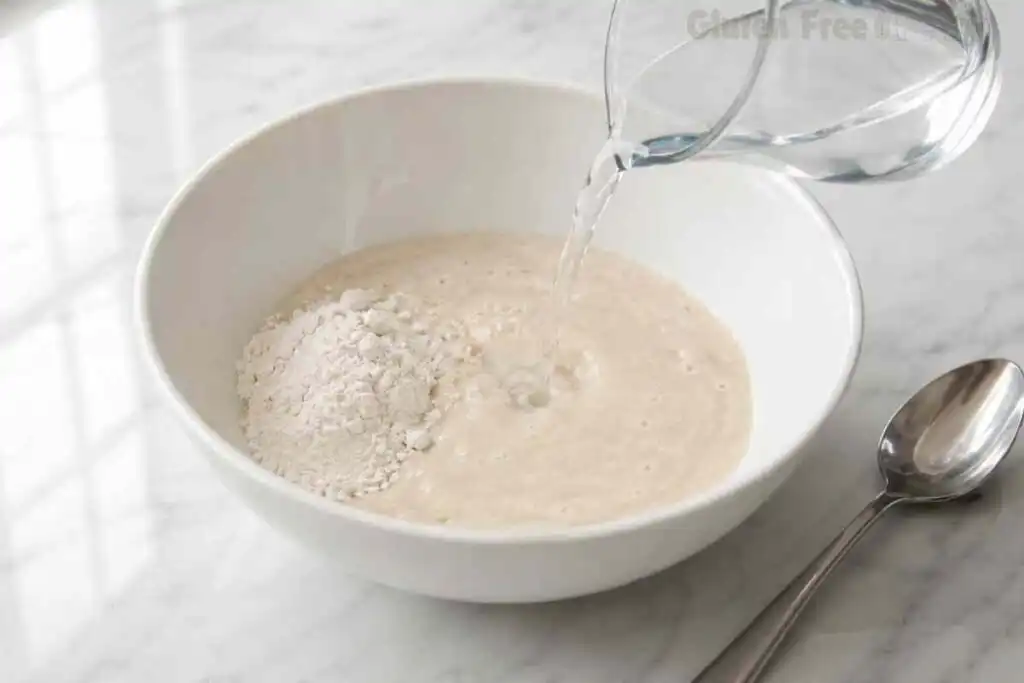 Filtered water being poured into gluten free flour starter during the daily feeding process.