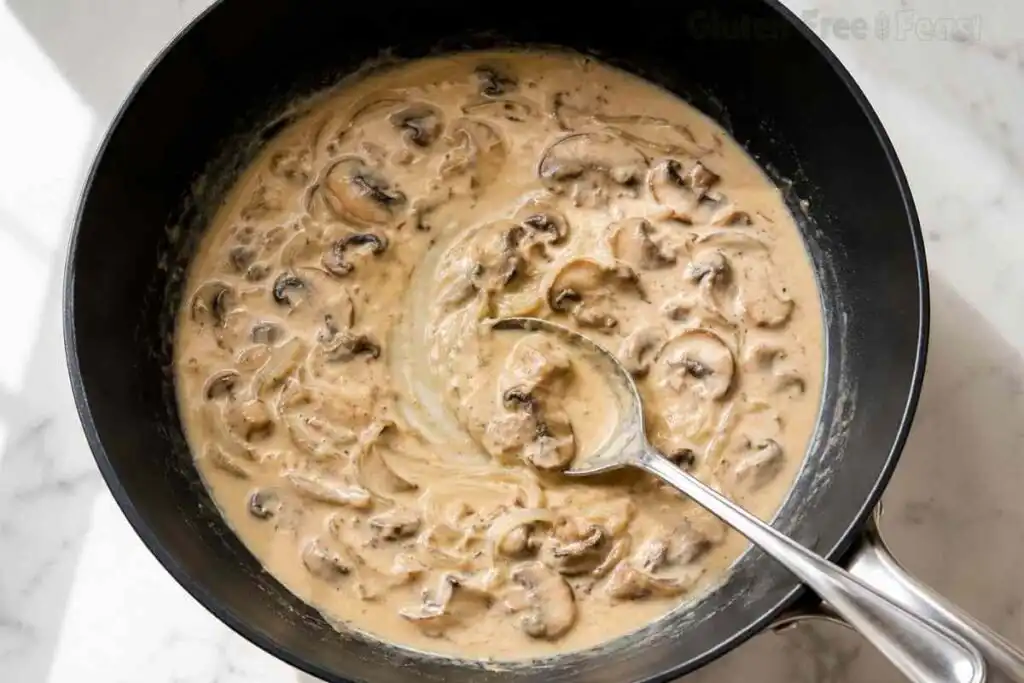 Creamy mushroom stroganoff sauce finished in a skillet before serving over gluten-free noodles.