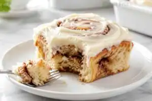 Frosted gluten free cinnamon roll served on a white plate