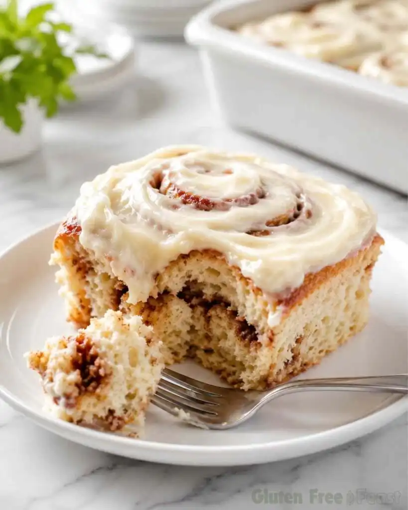 Single frosted gluten free cinnamon roll on a white plate