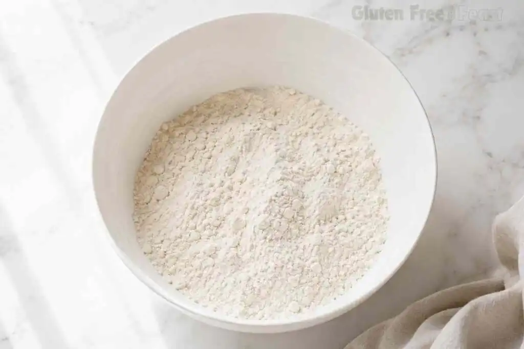 Gluten free flour mixture in a white mixing bowl on a marble countertop.
