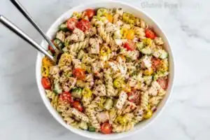 Gluten-free rotini pasta salad with chicken, tomatoes, cucumber, and pepperoncini in a white serving bowl