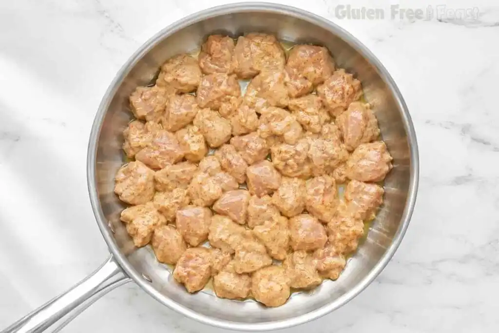Bite-sized marinated chicken thighs cooking in a stainless-steel skillet