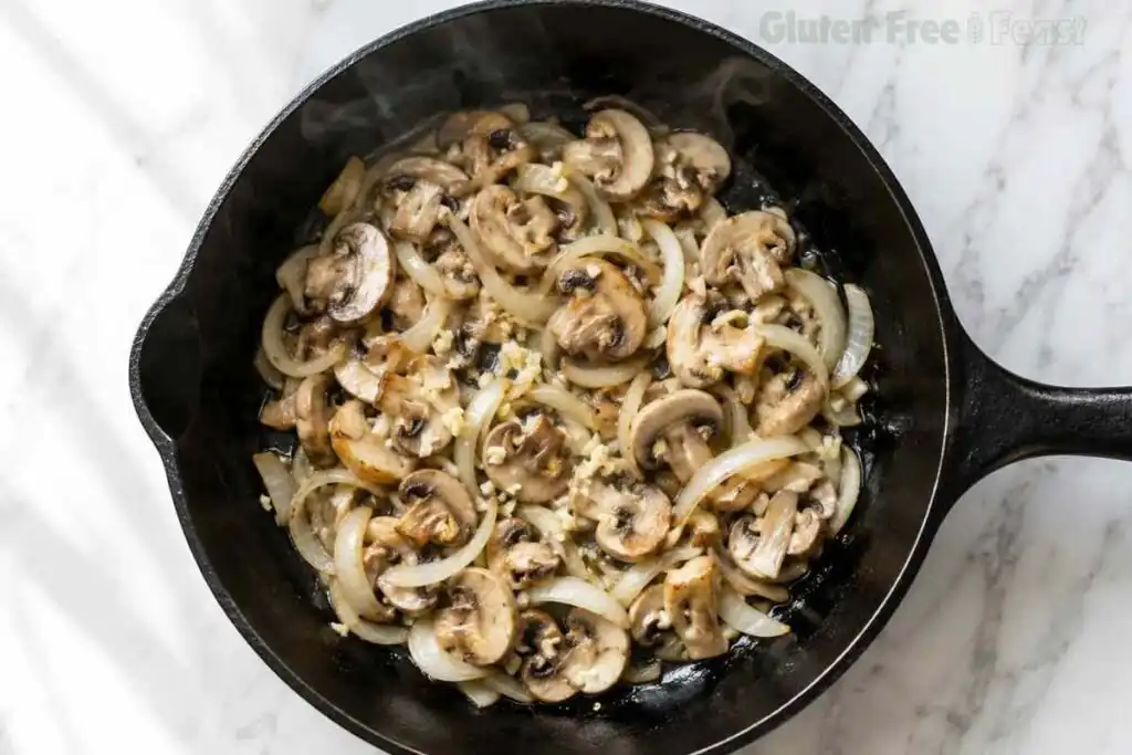 Mushrooms and onions sautéing in a skillet for Gluten Free Beef Stroganoff.