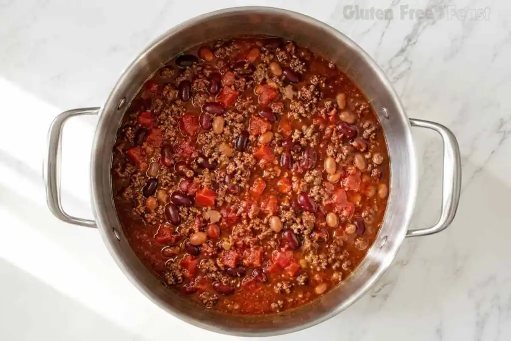 Gluten free chili simmering with beef, kidney beans, pinto beans, tomatoes, and sauce in a stainless steel pot.