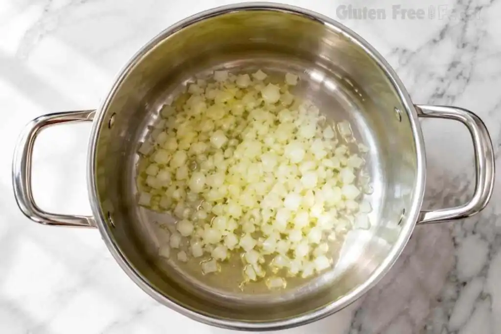 Diced onion cooking in olive oil inside a stainless steel pot for gluten free chili.