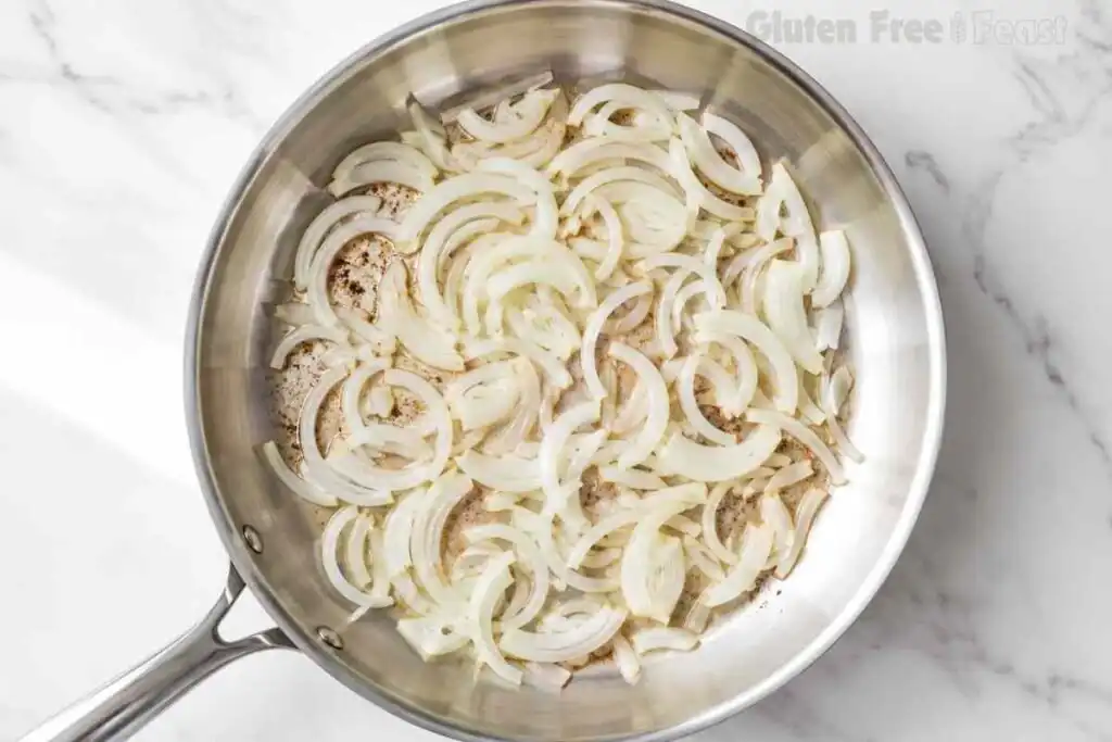 Thinly sliced onions sautéing in a stainless-steel skillet
