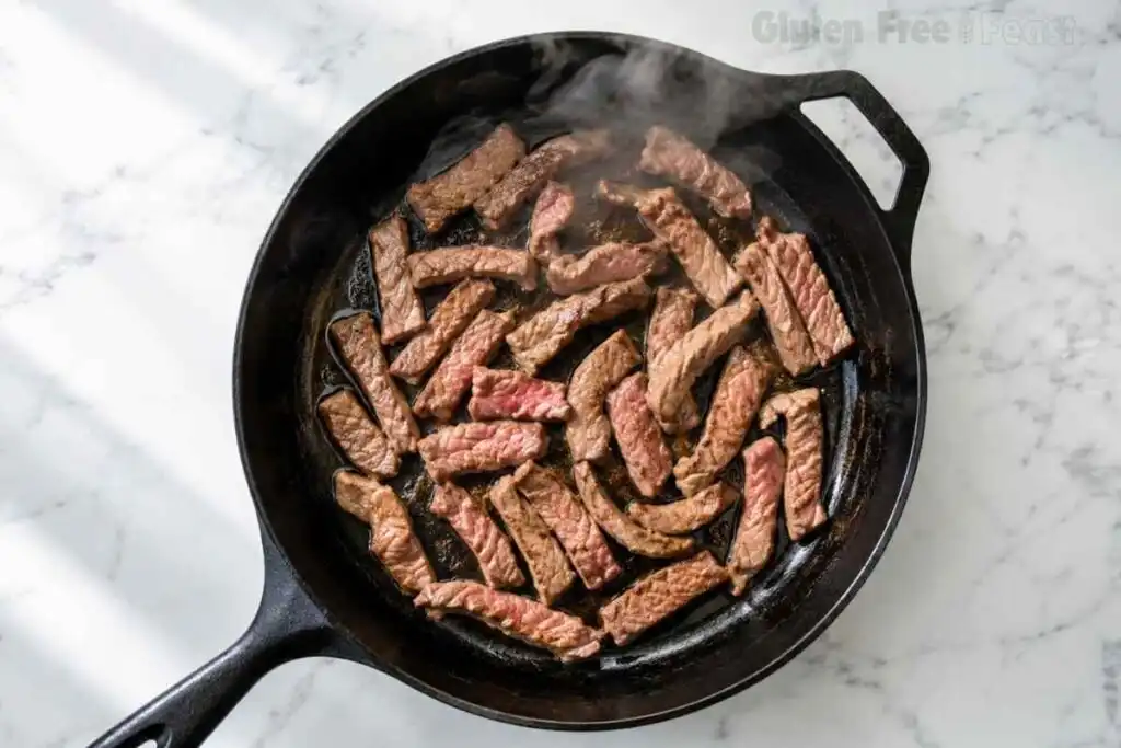 Beef strips browning in a cast iron skillet for Gluten Free Beef Stroganoff.