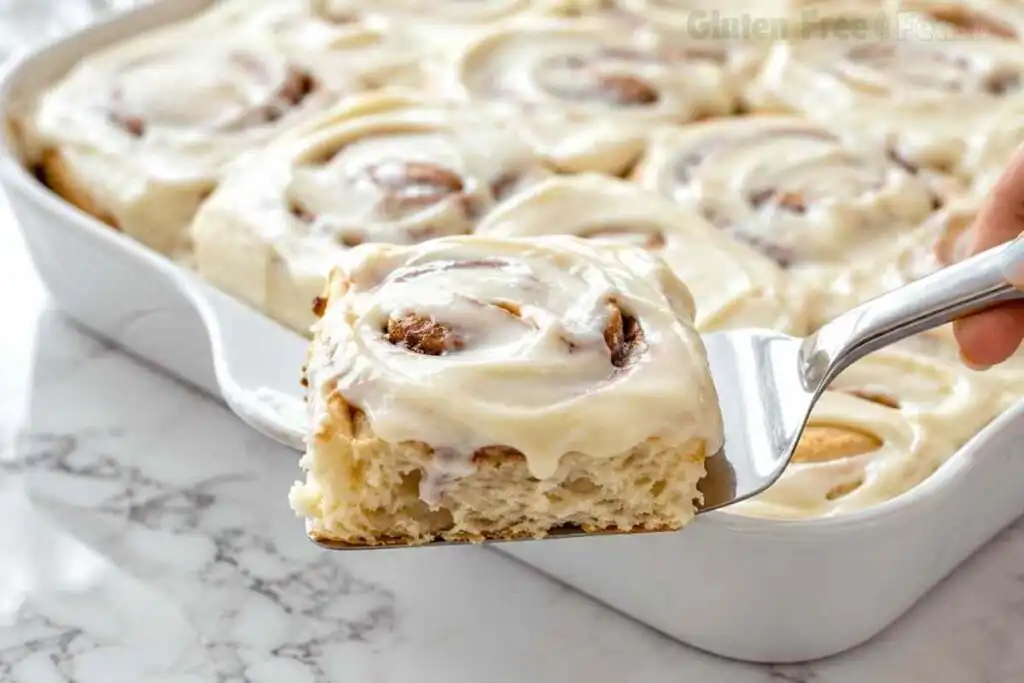 Frosted gluten free cinnamon roll lifted from baking dish with a fork
