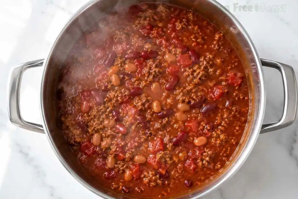 Thick gluten free chili simmering in a stainless steel pot with steam rising.